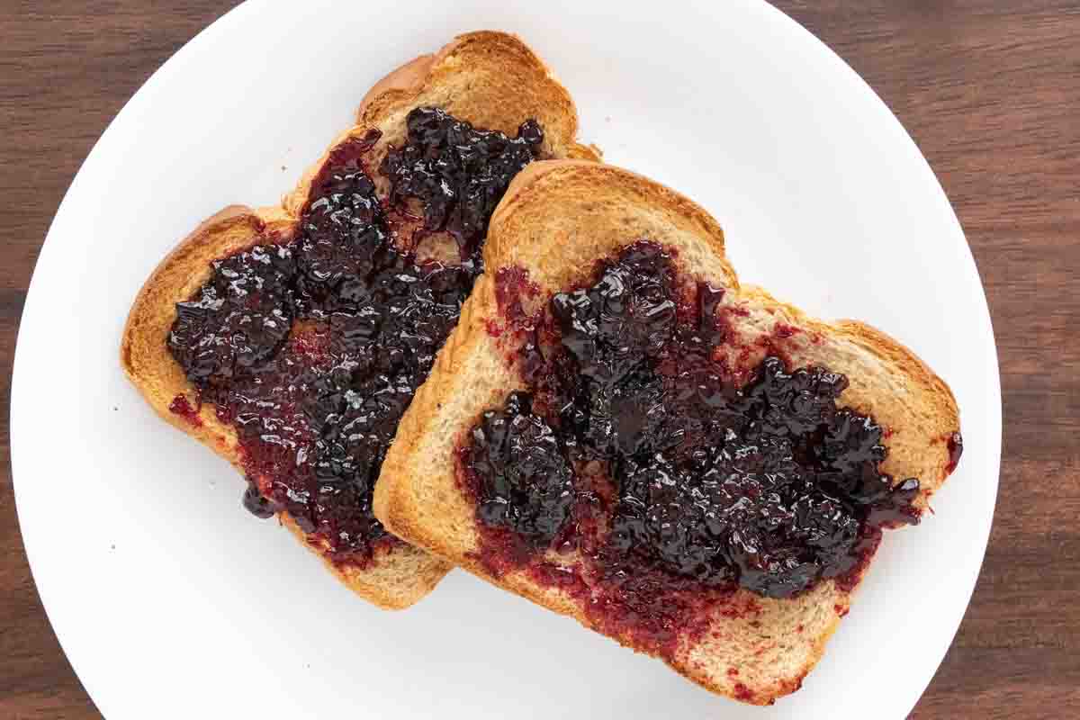 Blackberry jam on toast on a white plate.