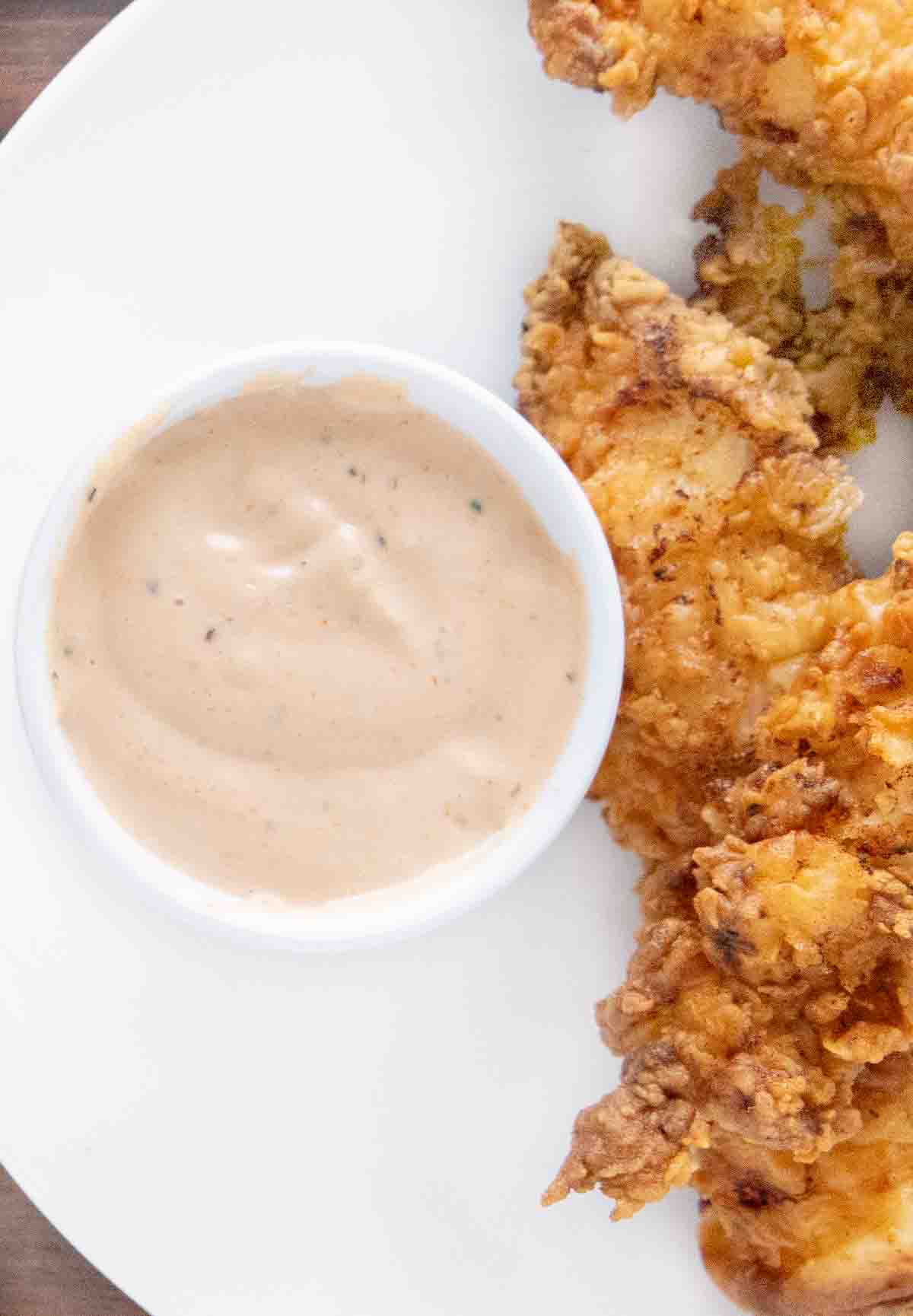 Cane's chicken sauce in a ramekin with fried chicken tenders on a white plate.
