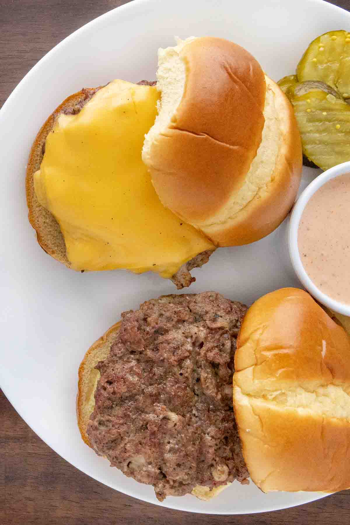 Two bison burgers on a white plate, one with cheese.