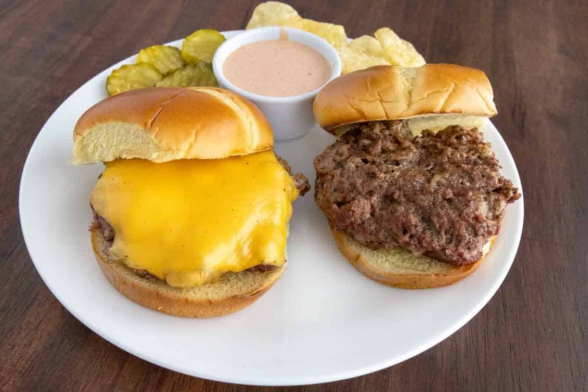 Two bison burgers on a white plate, one with cheese.