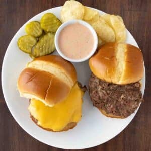 Two bison burgers on a white plate, one with cheese.