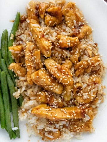 Bourbon chicken on a bed of rice on a white plate with green beans.