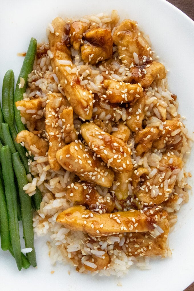 Bourbon chicken on a bed of rice on a white plate with green beans.