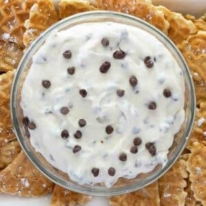 Cannoli dip in a glass bowl with pizzelle quarters on a white serving platter.