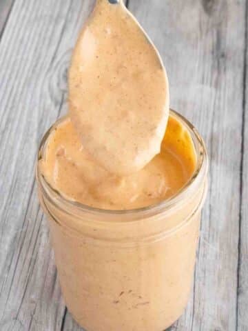 Chipotle mayonnaise in a glass jar with a spoon coming out.