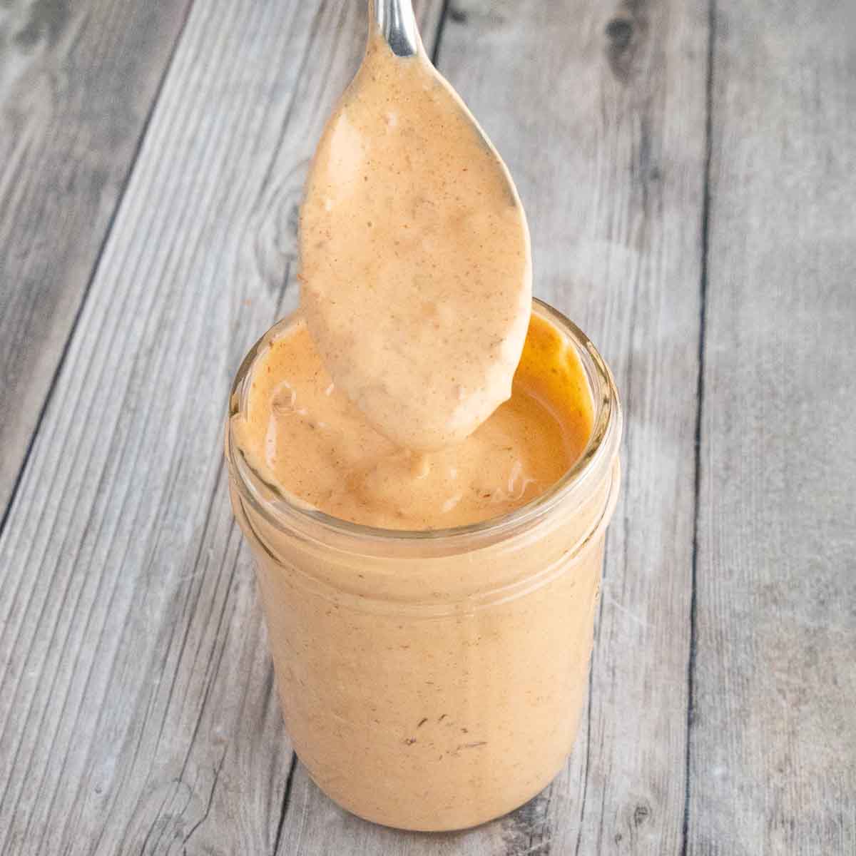 Chipotle mayonnaise in a glass jar with a spoon coming out.