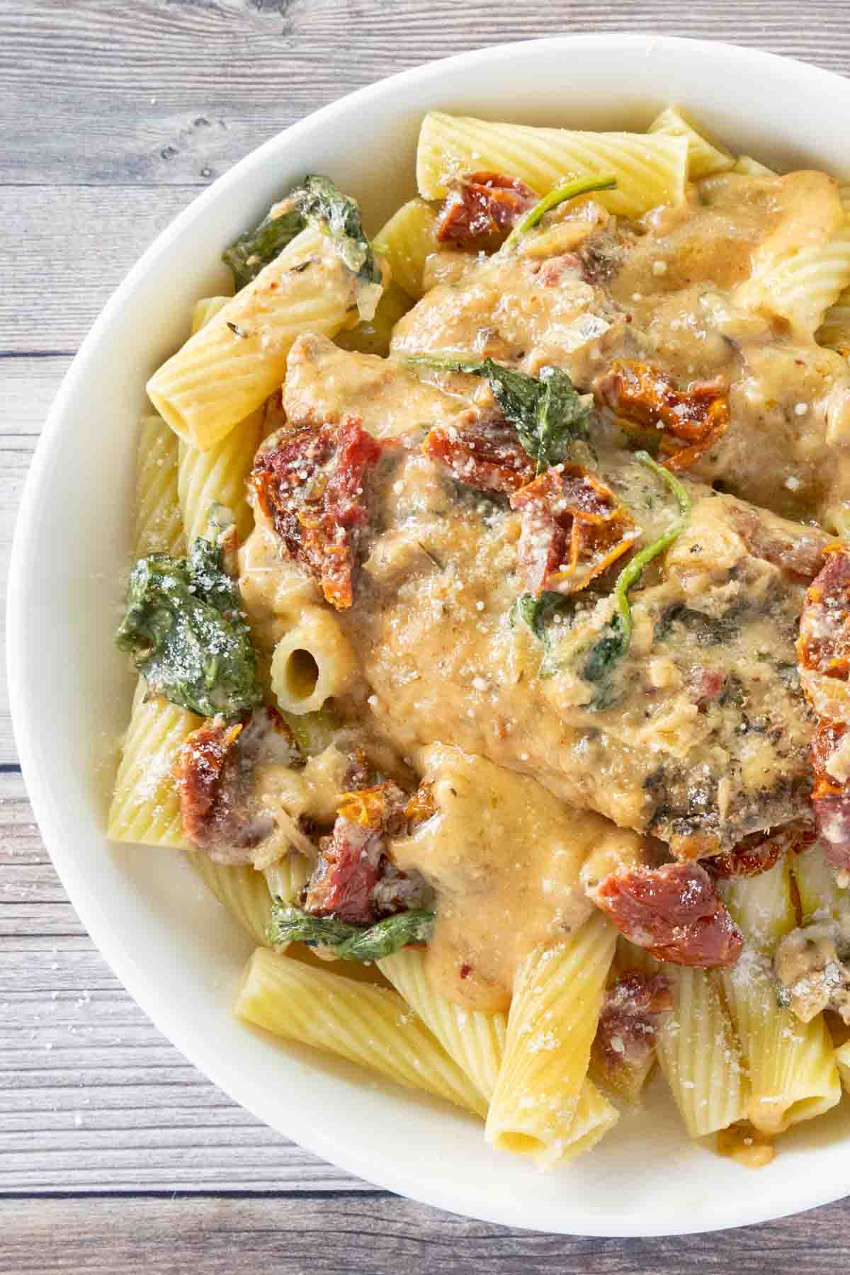 Crockpot tuscan chicken over rigatoni in a white bowl.