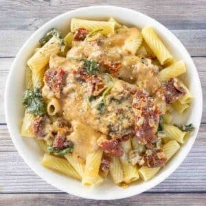 Crockpot tuscan chicken over rigatoni in a white bowl.