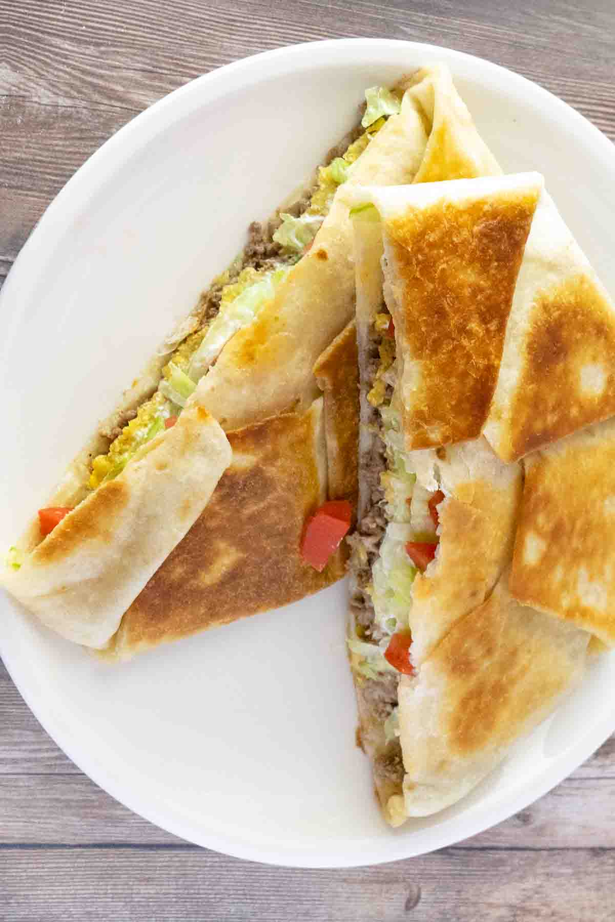 Finished homemade Crunchwrap Supreme recipe cut in half stacked on a white plate.