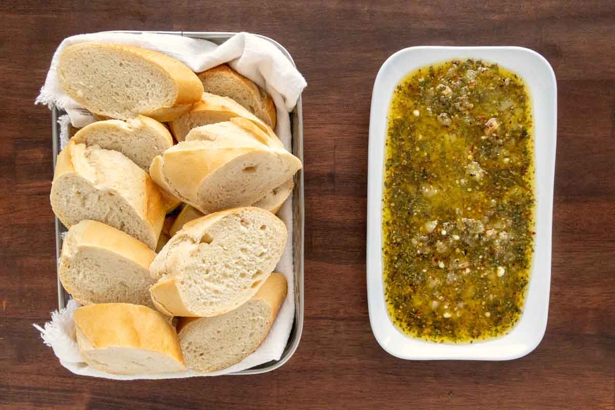 Olive oil bread dip on a white oblong platter with platter of sliced bread.