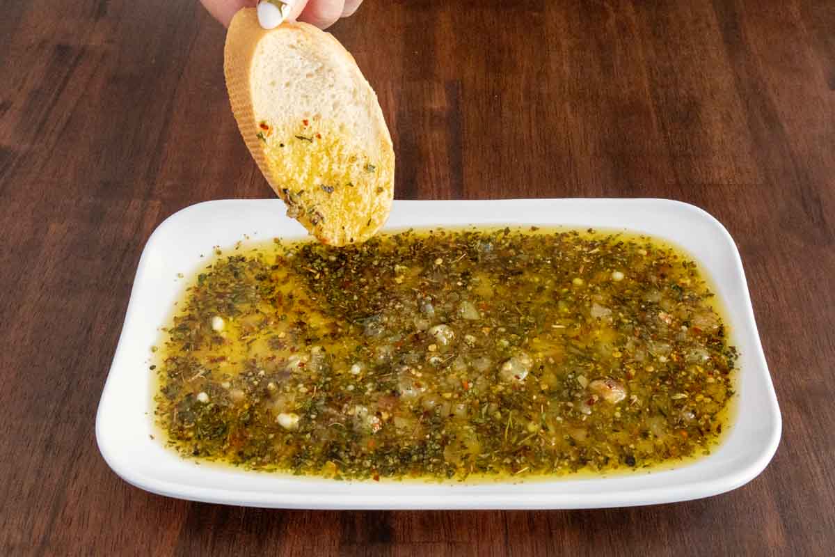 Hand holding a slice of bread dipping into the oilive oil bread dip.