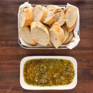 Olive oil bread dip on a white oblong platter with platter of sliced bread.