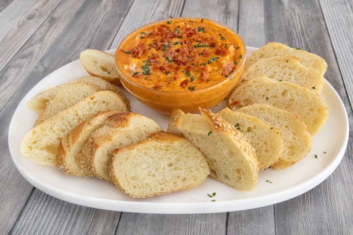 Pizza dip in a glass bowl on a white plate with bread slices.
