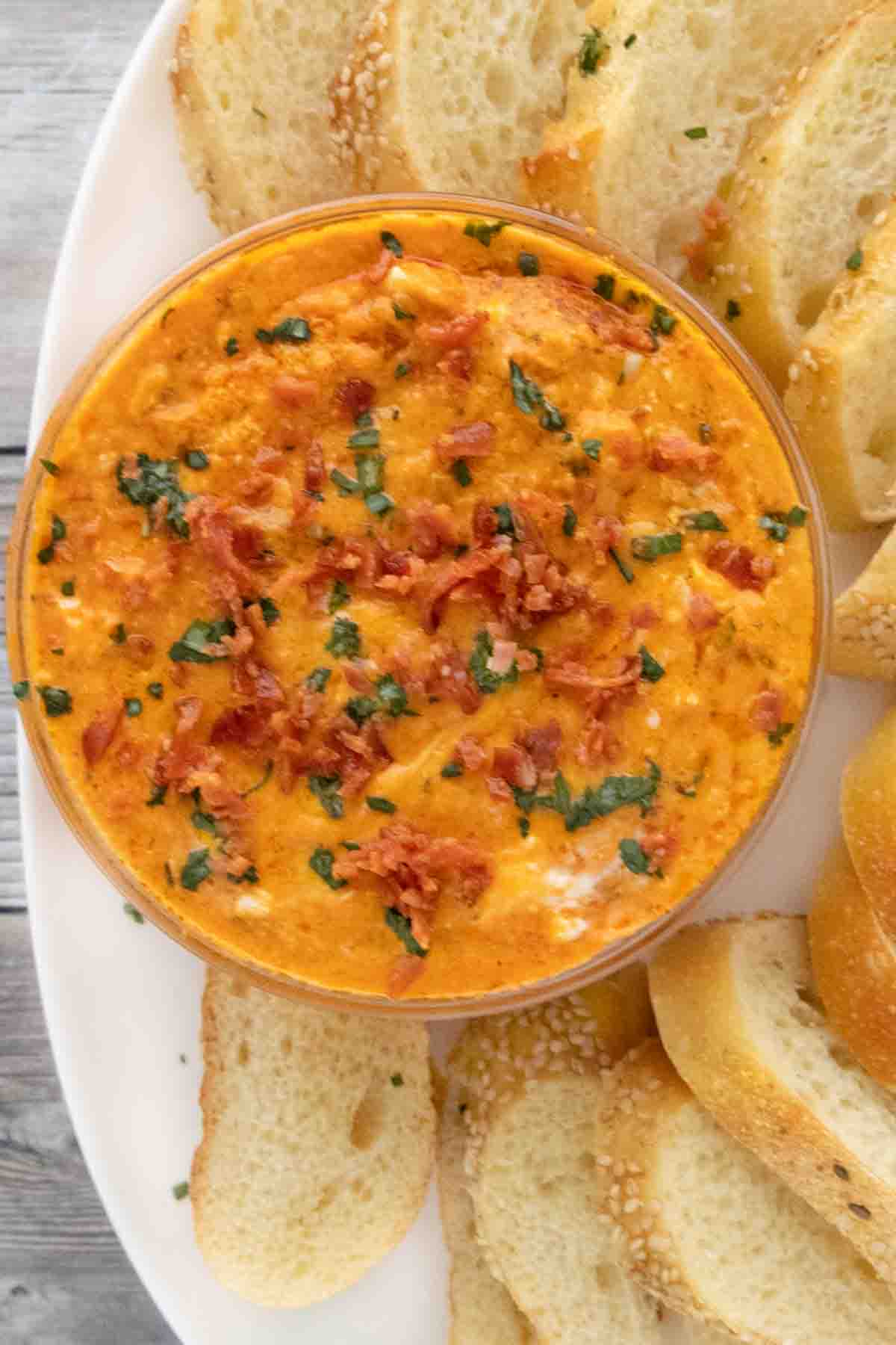 Pizza dip in a glass bowl on a white plate with bread slices.