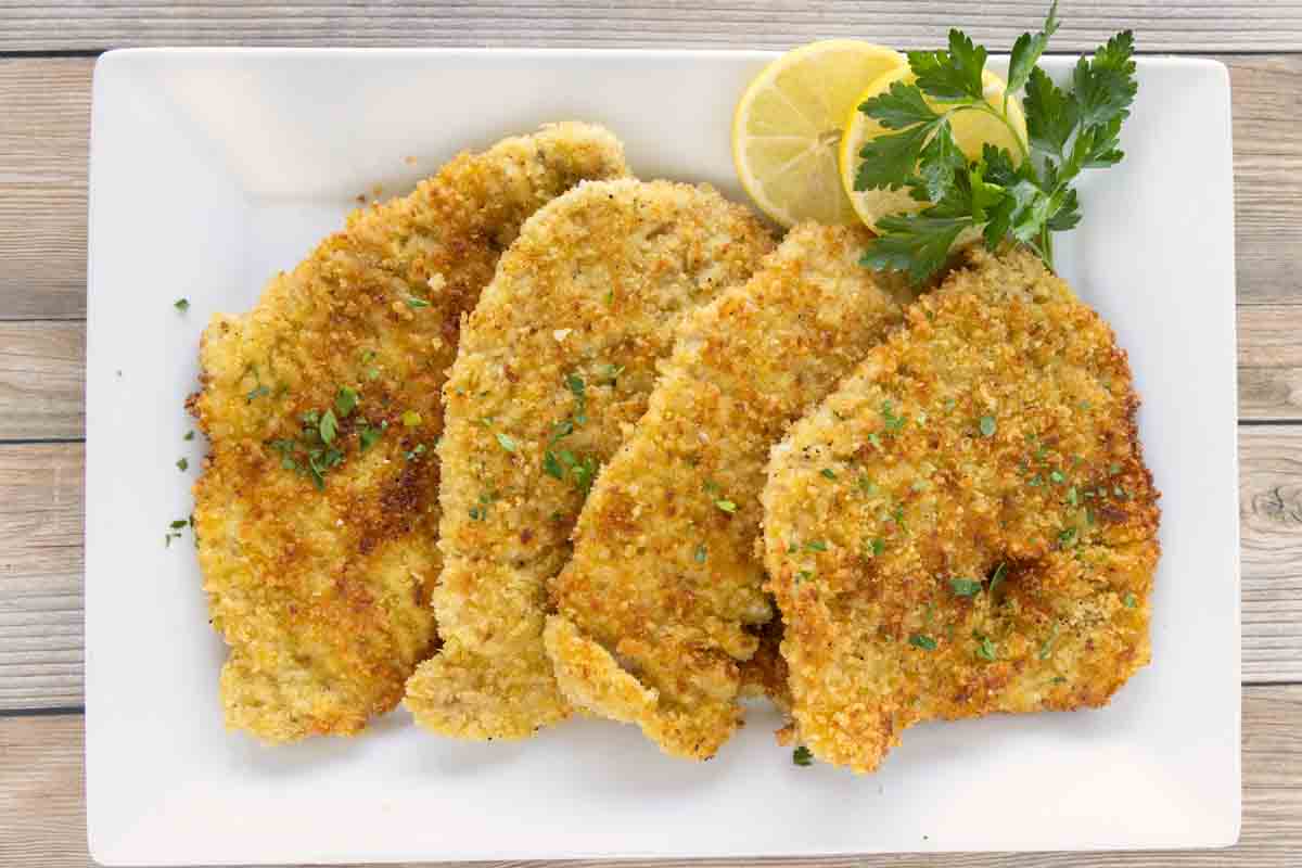 Pork schnitzel on a white platter with lemon circles and parsley.