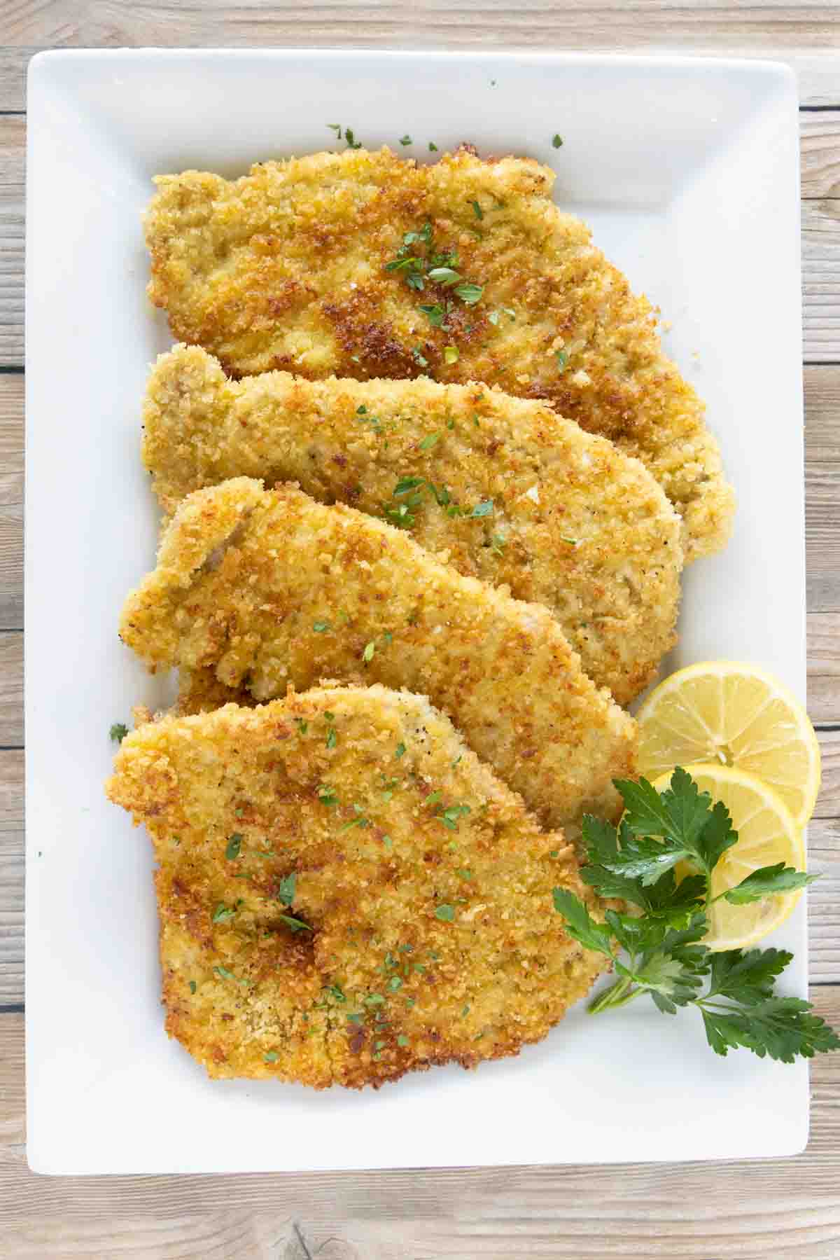 Pork schnitzel on a white platter with lemon circles and parsley.