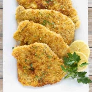 Pork schnitzel on a white platter with lemon circles and parsley.