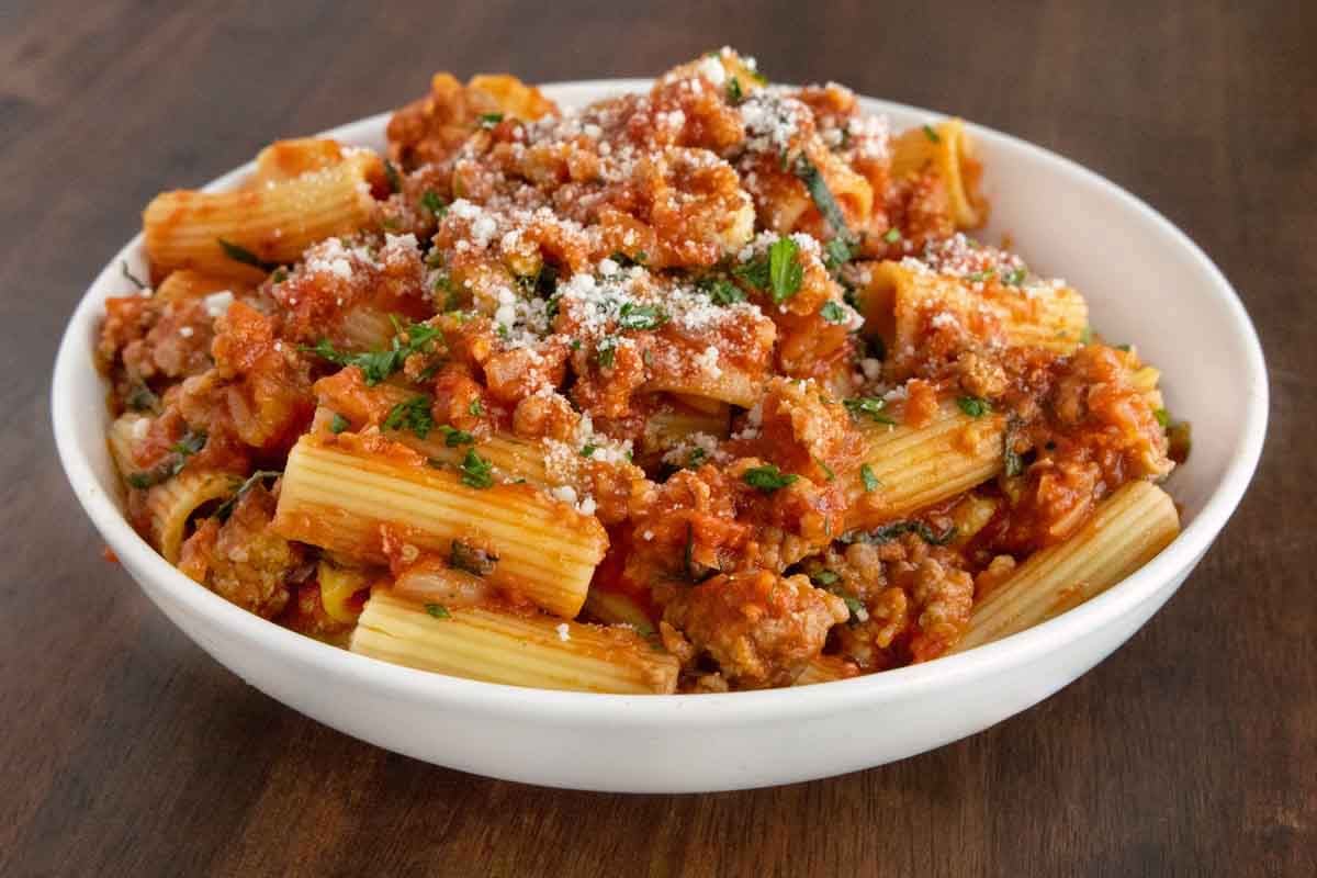Spicy Sausage Pasta in a white bowl garnished with chopped basil and grated cheese.