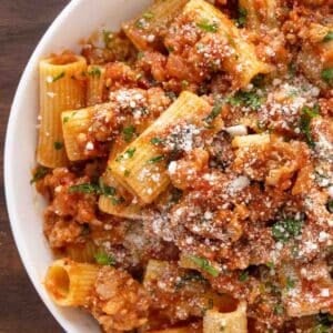 Spicy Sausage Pasta in a white bowl garnished with chopped basil and grated cheese.