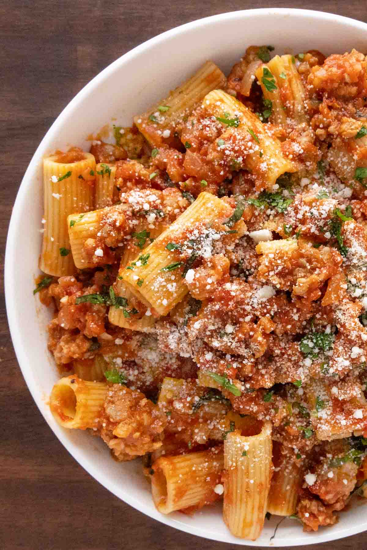 Spicy Sausage Pasta in a white bowl garnished with chopped basil and grated cheese.