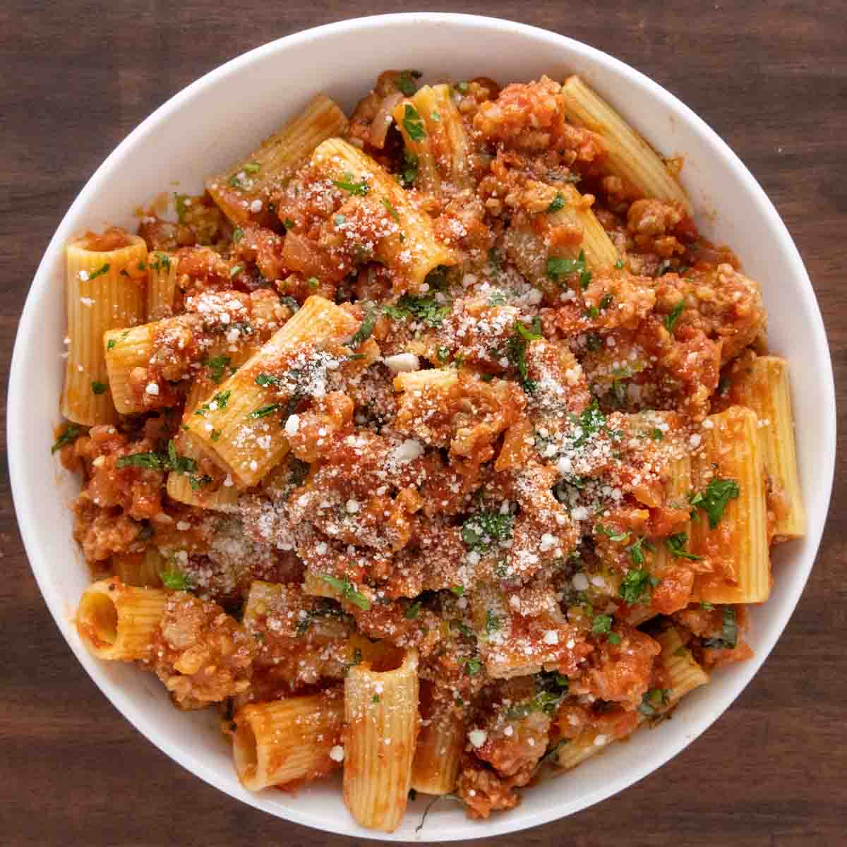 Spicy Sausage Pasta in a white bowl garnished with chopped basil and grated cheese.