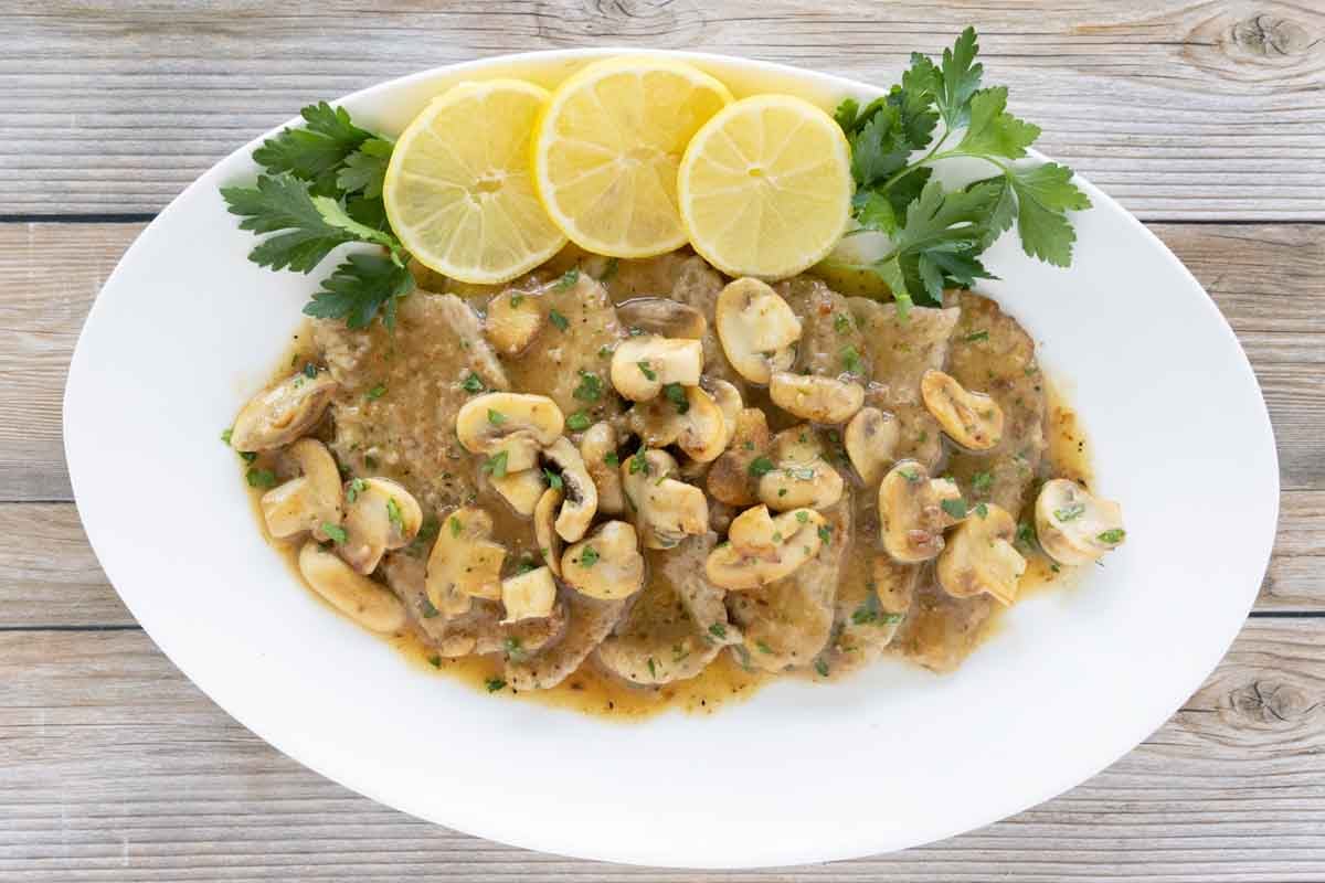 Veal scallopini with lemon circles and parsley on a white oval platter.