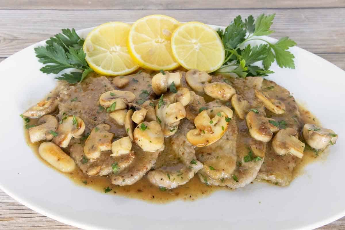 Veal scallopini with lemon circles and parsley on a white oval platter.