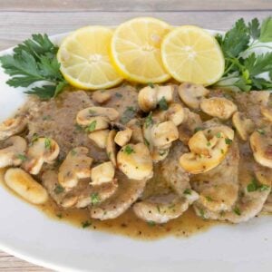 Veal scallopini with lemon circles and parsley on a white oval platter.