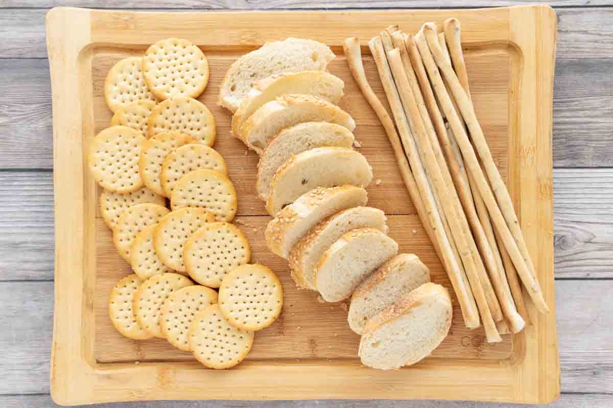 Crackers, breadsticks and sliced baguettes on a cutting board.