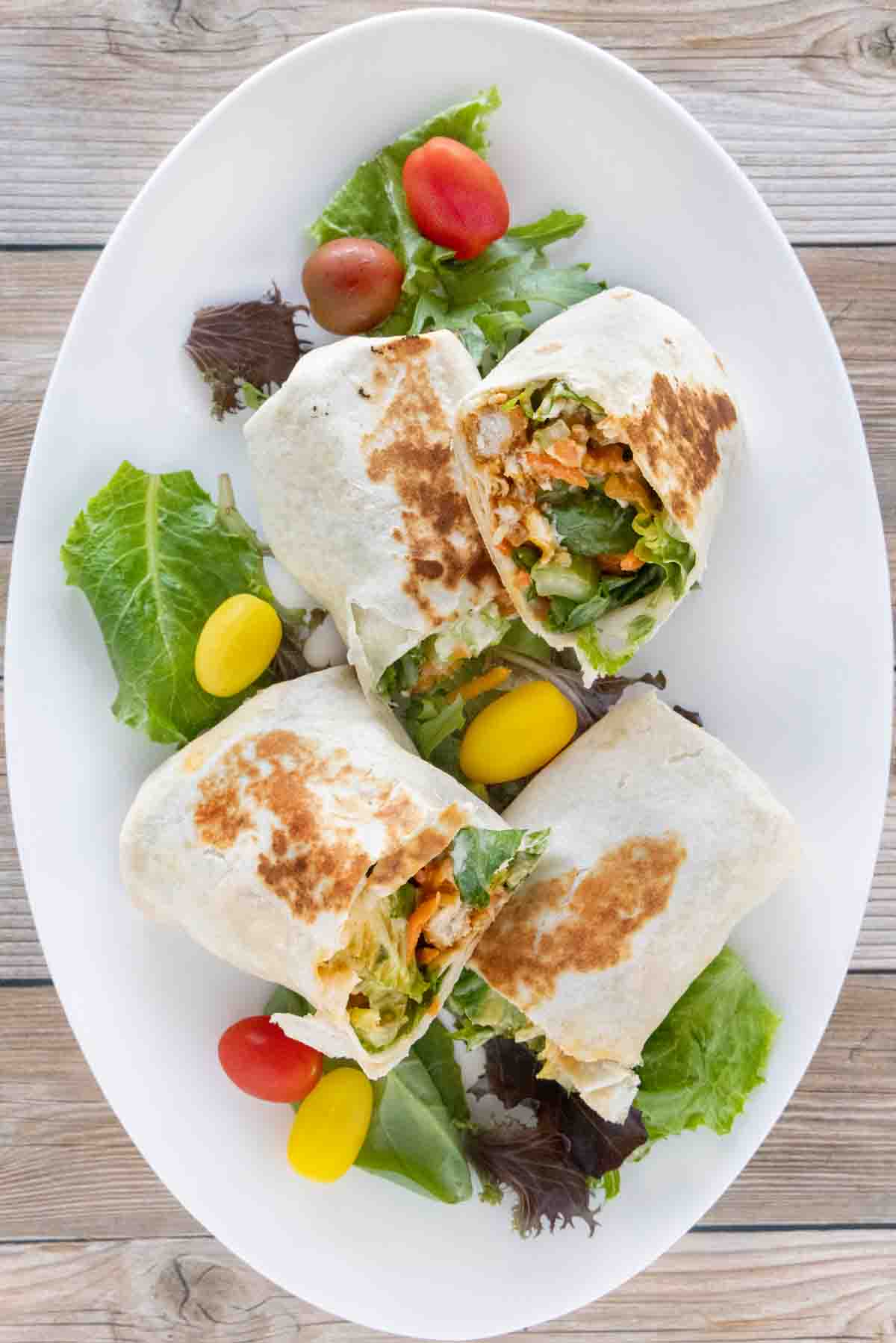 Two buffalo chicken wraps cut in half and stacked on a white platter.