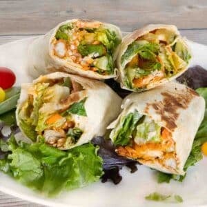 Two buffalo chicken wraps cut in half and stacked on a white platter.