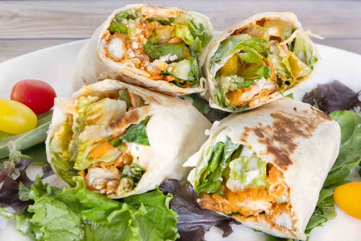 Two buffalo chicken wraps cut in half and stacked on a white platter.
