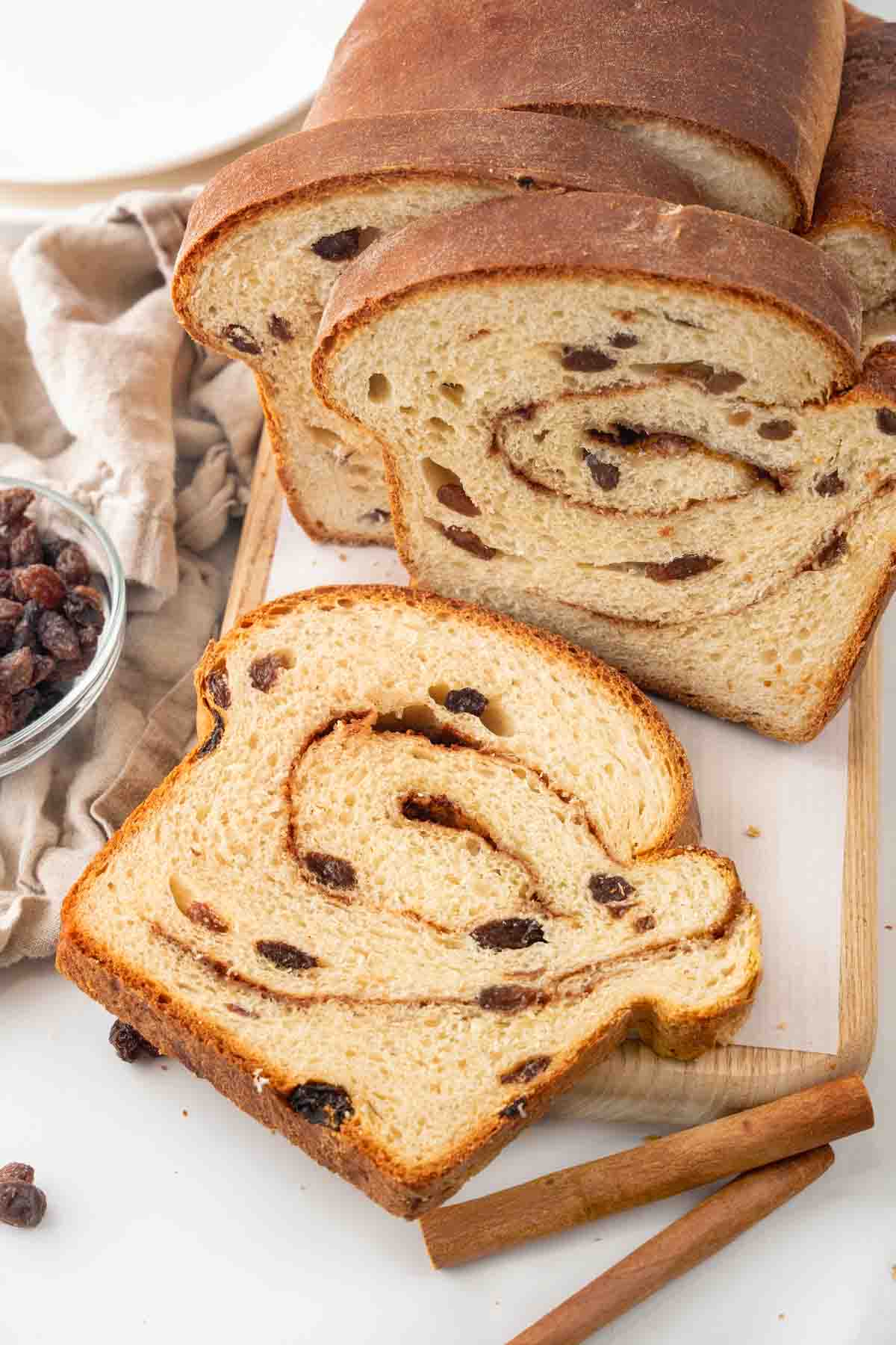 Slices of cinnamon raisin bread against the loaf on a cutting board.