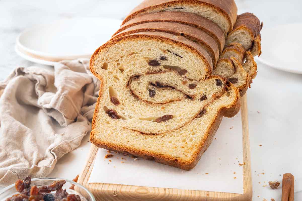 Slices of cinnamon raisin bread against the loaf on a cutting board.