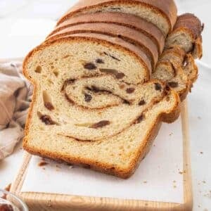 Slices of cinnamon raisin bread against the loaf on a cutting board.