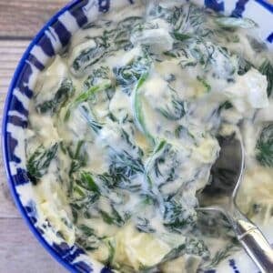Creamed spinach in a blue and white bowl, with a spoon in it.