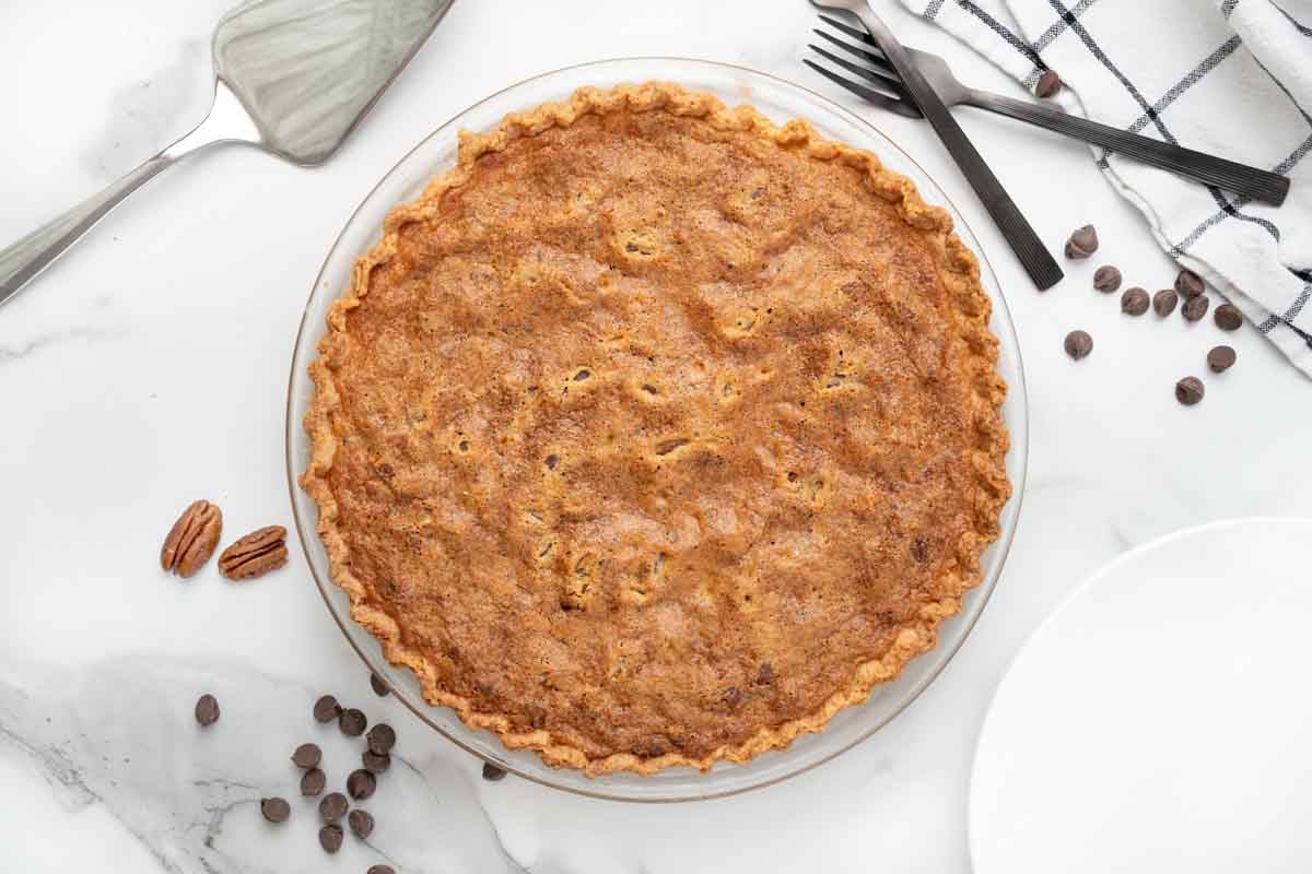 Baked derby pie, with pie spatula, pecans and chocolate chips placed around it.