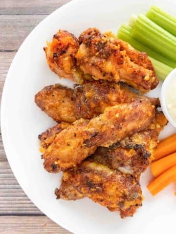 Mango Habanero wings on a white plate with a dip, celery and carrot sticks.