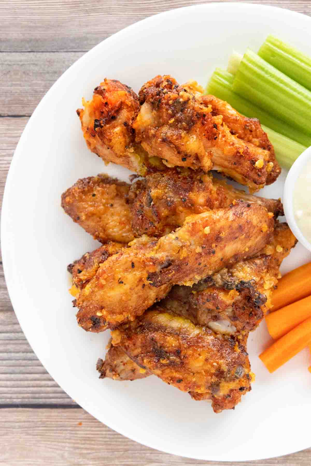 Mango Habanero wings on a white plate with a dip, celery and carrot sticks.