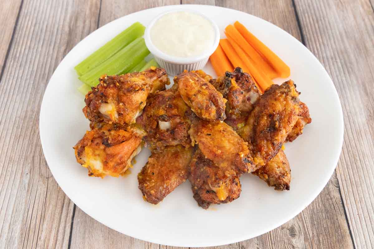 Mango Habanero wings on a white plate with a dip, celery and carrot sticks.