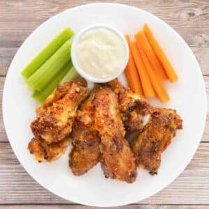 Mango Habanero wings on a white plate with a dip, celery and carrot sticks.