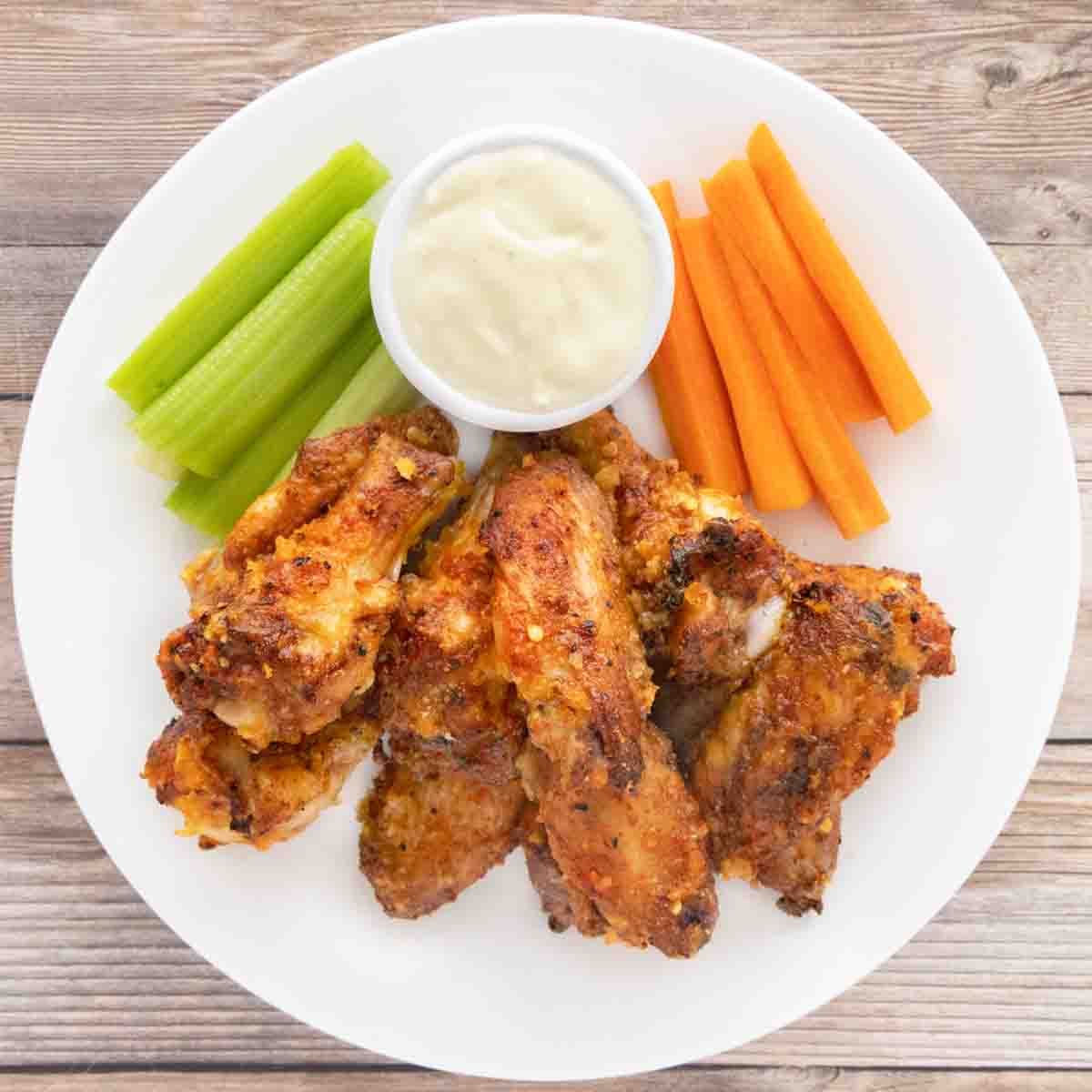 Mango Habanero wings on a white plate with a dip, celery and carrot sticks.