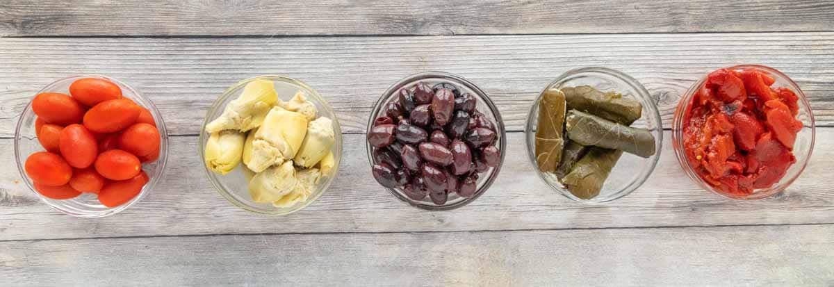 olives, stuffed grape leaves and vegetables in five small bowls.