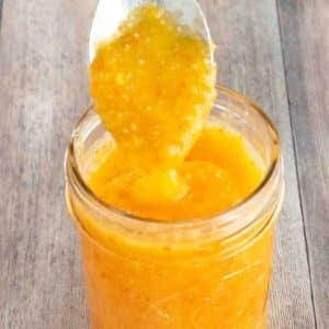 Mango habanero sauce in a glass jar with a spoon coming out.