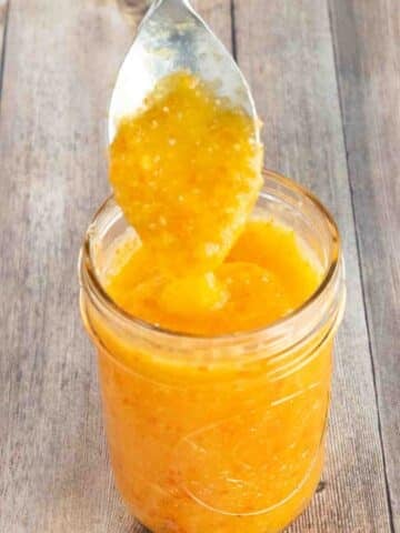 Mango habanero sauce in a glass jar with a spoon coming out.