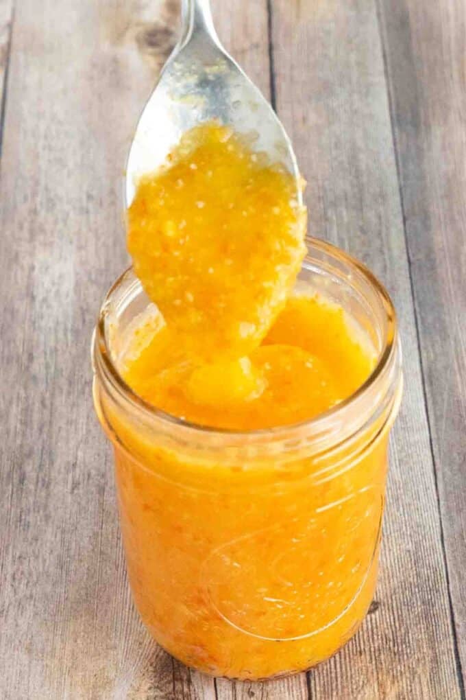 Mango habanero sauce in a glass jar with a spoon coming out.