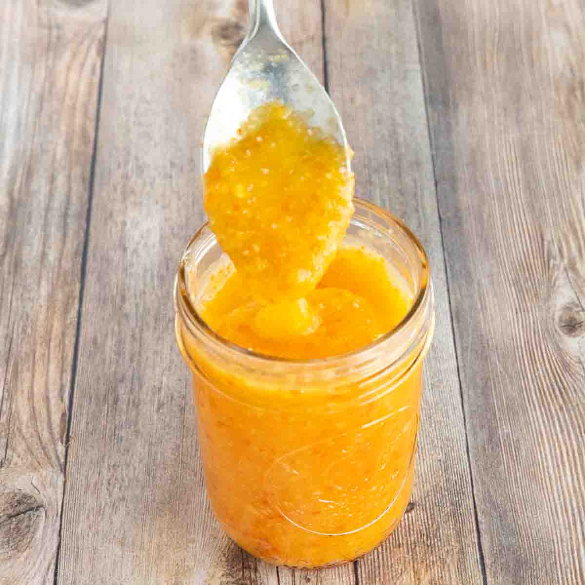 Mango habanero sauce in a glass jar with a spoon coming out.