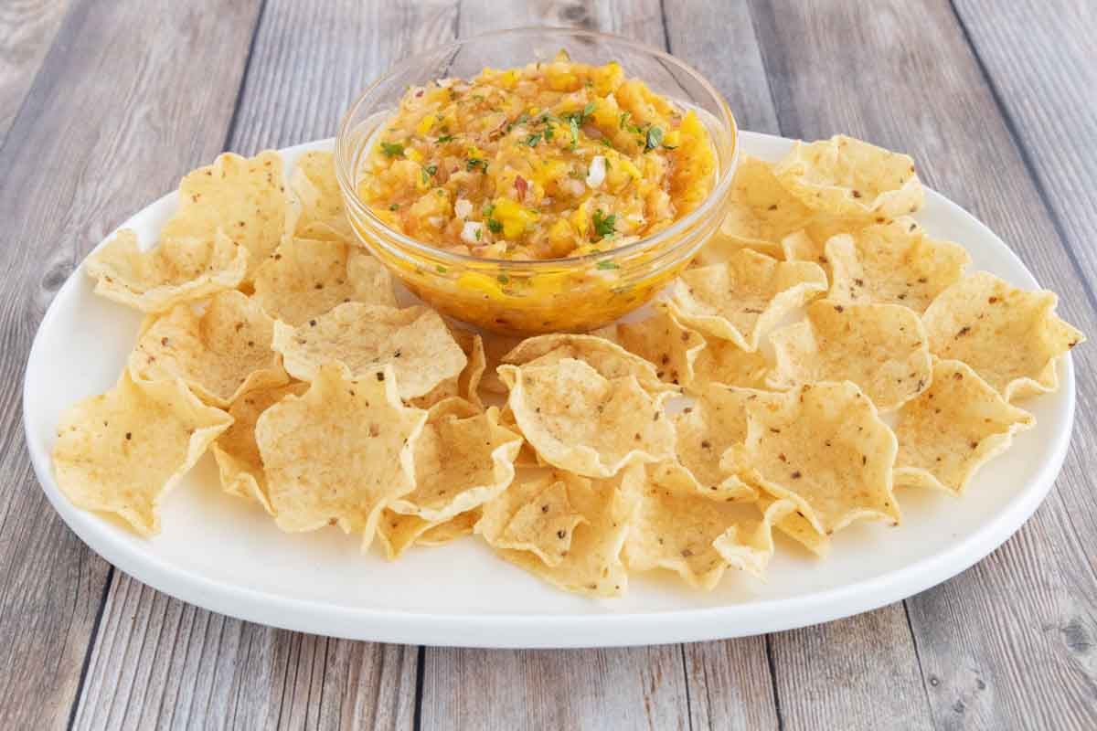 Mango salsa and tortilla chips on a white platter.