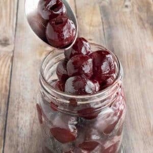 A spoon coming out of a jar of maraschino cherries.