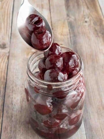 A spoon coming out of a jar of maraschino cherries.
